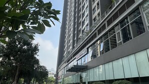 A modern high-rise building with a glass facade, a well-maintained sidewalk, and surrounding greenery. - Vinhomes Gardenia - 2 Brs Apartment (Hanoi)