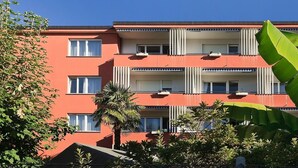 Un edificio de varios pisos con balcones, unidades de aire acondicionado y fachada roja.