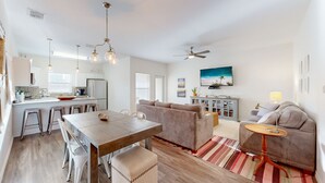 A spacious living area with a wooden dining table, a sofa, and a TV. - Shared Heated Pool, Golf Cart Access, Parking for 2, Pet Friendly (Port Aransas)
