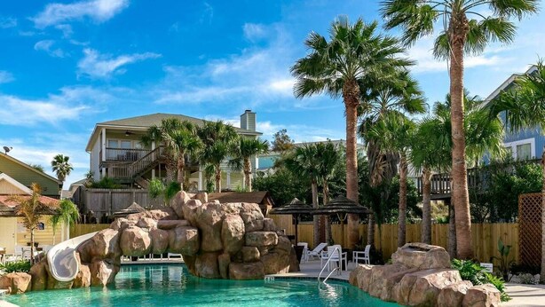 A pool area with a rock formation and palm trees. - Shared Heated Pool, Golf Cart Access, Parking for 2, Pet Friendly (Port Aransas)