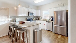 A modern kitchen with white cabinets, stainless steel appliances, and a central island with stools. - Shared Heated Pool, Golf Cart Access, Parking for 2, Pet Friendly (Port Aransas)