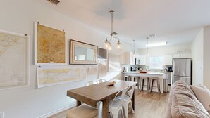 A modern kitchen with a dining area, featuring a wooden table, white chairs, and a beige sofa. - Shared Heated Pool, Golf Cart Access, Parking for 2, Pet Friendly (Port Aransas)