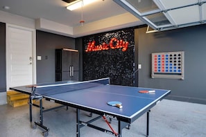 Una mesa de ping pong con un letrero de neón que dice 'Music City' al fondo.