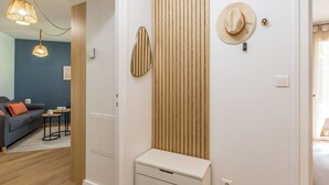 A hallway with a wooden slat wall, a small white cabinet, and a hat on the wall. There is a blue sofa and a table with cups in the background. - Ermitage by Interhome (Hossegor)