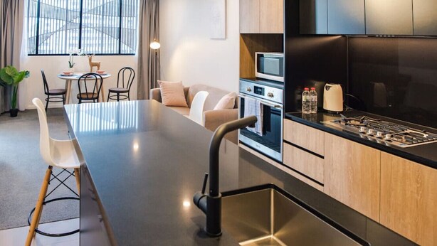 A modern kitchen with a central island, built-in oven, microwave, and gas stove. - Ideal Cozy 1BR for your Urban Escape in Gabba (Woolloongabba)