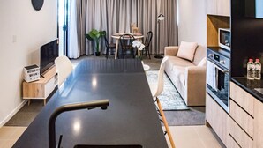 A modern kitchen with a central island, a dining area with a round table, and a living space with a sofa. - Ideal Cozy 1BR for your Urban Escape in Gabba (Woolloongabba)