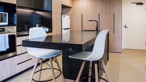 A modern kitchen with a black countertop, two white chairs, and a white refrigerator. - Ideal Cozy 1BR for your Urban Escape in Gabba (Woolloongabba)