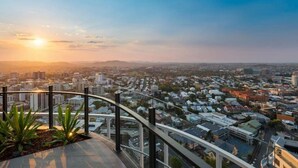 A cityscape at sunset with a view from a balcony overlooking a densely populated area with various buildings and a clear sky. - Stunning 1BD Haven with Panoramic City Views (Brisbane City)