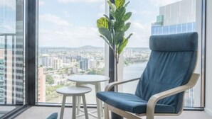 A modern room with a large window, a blue chair, a small round table, and a shark plush toy. - Stunning 1BD Haven with Panoramic City Views (Brisbane City)