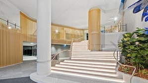 A modern interior with a central staircase, white columns, and vertical wooden slats. - Stunning 1BD Haven with Panoramic City Views (Brisbane City)