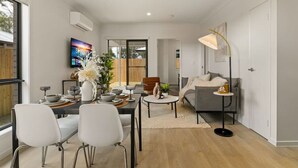Un salon moderne comprenant un coin repas, un canapé gris, une table basse et un téléviseur fixé au mur.