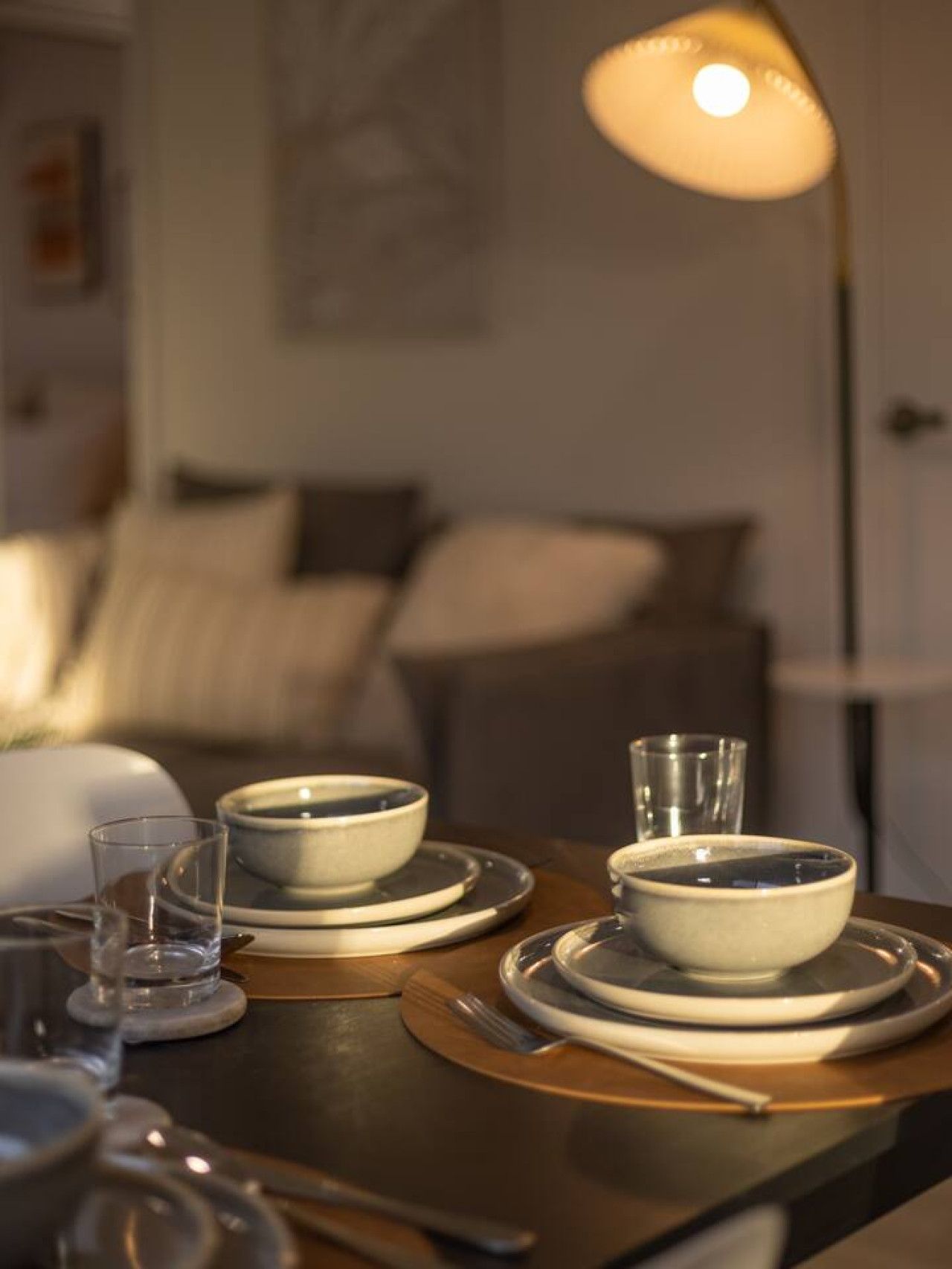 Une table à manger dressée avec des assiettes, des bols et des couverts, et une lampe sur pied en arrière-plan.