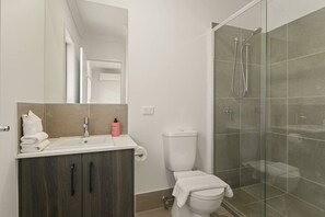 A modern bathroom with a glass shower enclosure, a white sink, and a dark wood vanity. - Dual-key 5BR Family home w/ stunning interior (Browns Plains)
