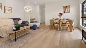 A modern living room with a sofa, coffee table, and dining area with chairs and a table. - Comfortable 3BR home/ Convenient location (Browns Plains)