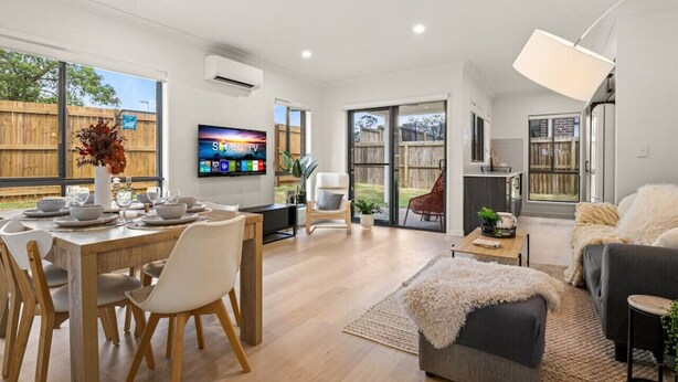 A spacious living area with a dining table set for six, a sofa, a TV mounted on the wall, and a sliding glass door leading to a patio. - Comfortable 3BR home/ Convenient location (Browns Plains)