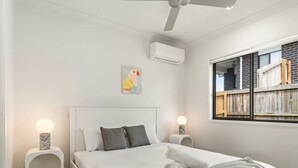Camera da letto con un letto, comodini, condizionatore d'aria, ventola a soffitto, una finestra con mensole per libri e un quadro appeso al muro.