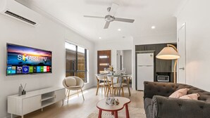 Un soggiorno moderno con una TV a schermo piatto, un divano, un tavolo da pranzo e una ventola a soffitto.