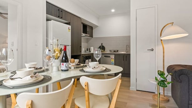 Una cucina moderna con mobili bianchi, una zona pranzo con sedie bianche e un divano grigio.