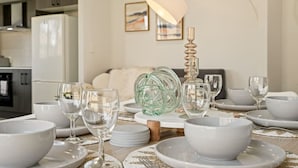 Una mesa de comedor dispuesta con cuencos, platos y copas de vino blancos, un florero de cristal decorativo y un candelabro alto.
