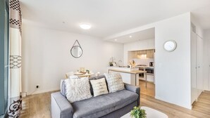 Uma sala de estar moderna com um sofá cinza, uma mesa de centro e uma cozinha ao fundo.