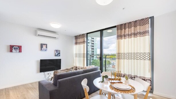 Uma sala de estar moderna com sofá, mesa de jantar com cadeiras, televisão de tela plana e uma grande janela com cortinas.