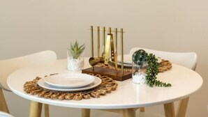Uma mesa de jantar redonda com um prato branco, uma pequena planta em vaso e um objeto decorativo.