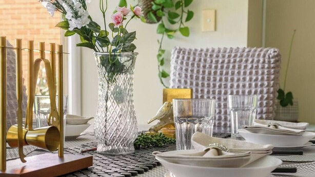 Una mesa de comedor dispuesta con platos, vasos y un jarrón con flores.