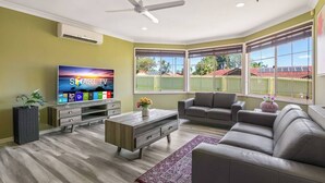 Una sala de estar con televisor de pantalla plana, sofás grises, una mesa de centro y un ventilador de techo.
