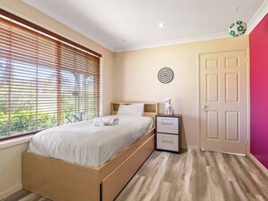 Quarto com uma cama, mesa de cabeceira, porta e janela com persianas.