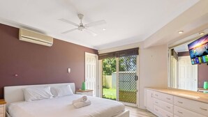 Un dormitorio con cama, ventilador de techo, televisión y puerta corrediza de vidrio al exterior.