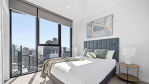 A modern bedroom with a large bed, a city view, a grey headboard, and a small bedside table with a lamp. - River&Ocean View Luxury 2BD Apt amazing Location (Broadbeach)