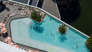 An aerial view of a swimming pool with lounge chairs and umbrellas, surrounded by a building. - River&Ocean View Luxury 2BD Apt amazing Location (Broadbeach)