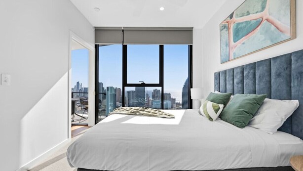 A modern bedroom with a city view, a large bed, and a cityscape visible through the windows. - River&Ocean View Luxury 2BD Apt amazing Location (Broadbeach)