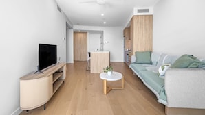 A modern living room with a flat-screen TV, a round coffee table, a sofa, and a kitchen area in the background. - River&Ocean View Luxury 2BD Apt amazing Location (Broadbeach)