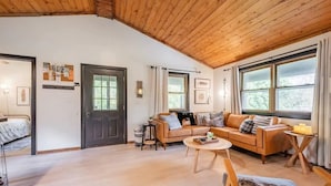 Un salón acogedor con techo de madera, un conjunto de sofá, una mesa de centro y una puerta que da a otra habitación.