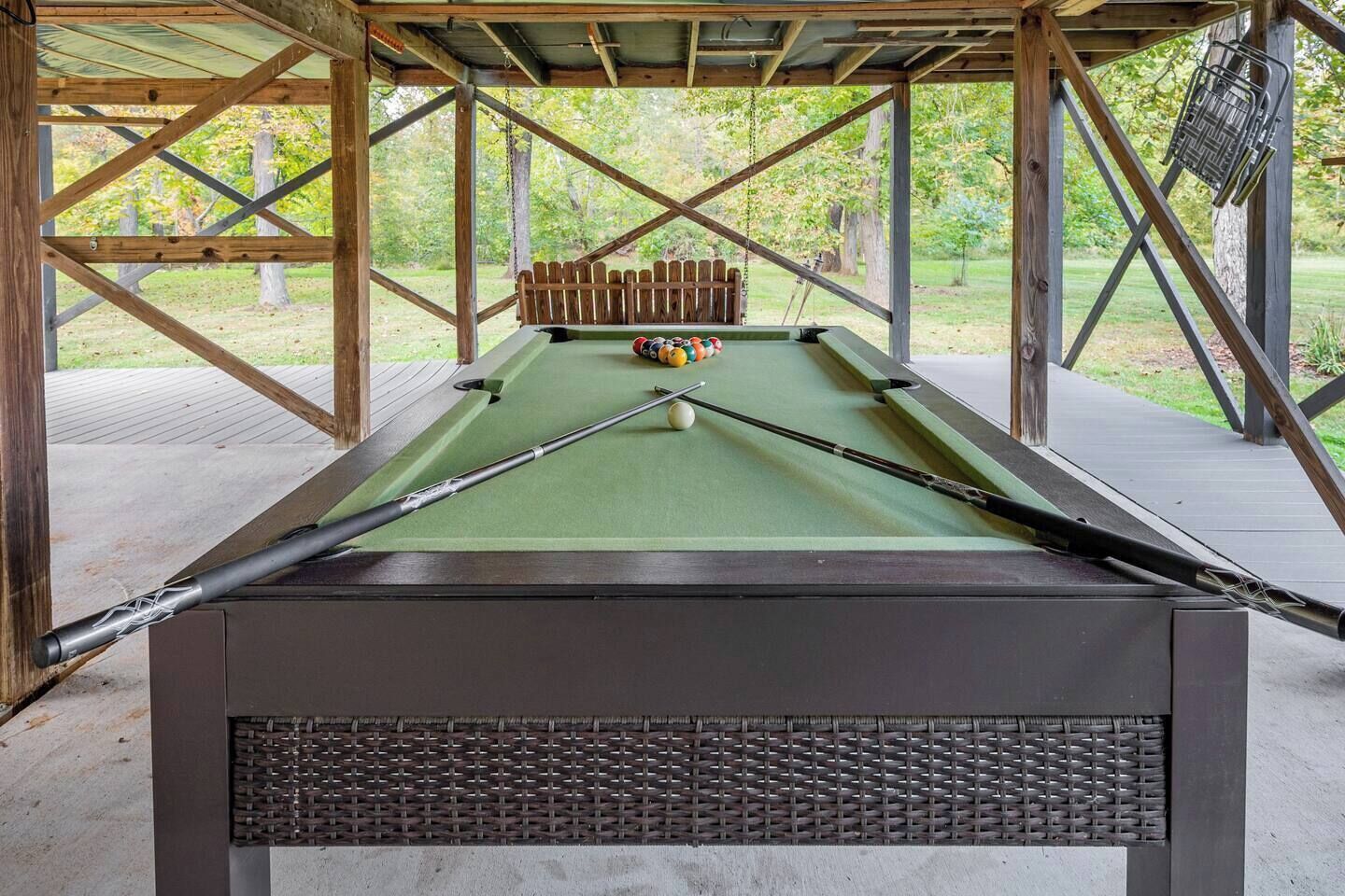 Une table de billard recouverte d’un drap vert, entourée d’une structure en bois formant une sorte de terrasse.