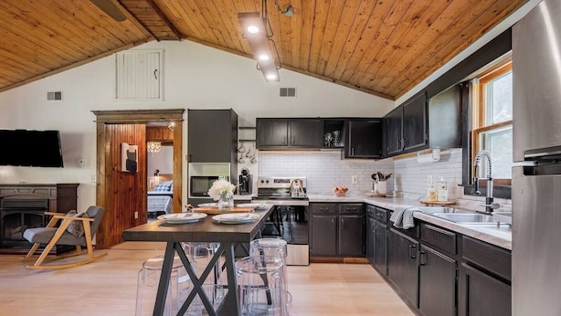 Una cocina moderna con armarios oscuros, un refrigerador de acero inoxidable y un comedor con una mesa y sillas de madera.