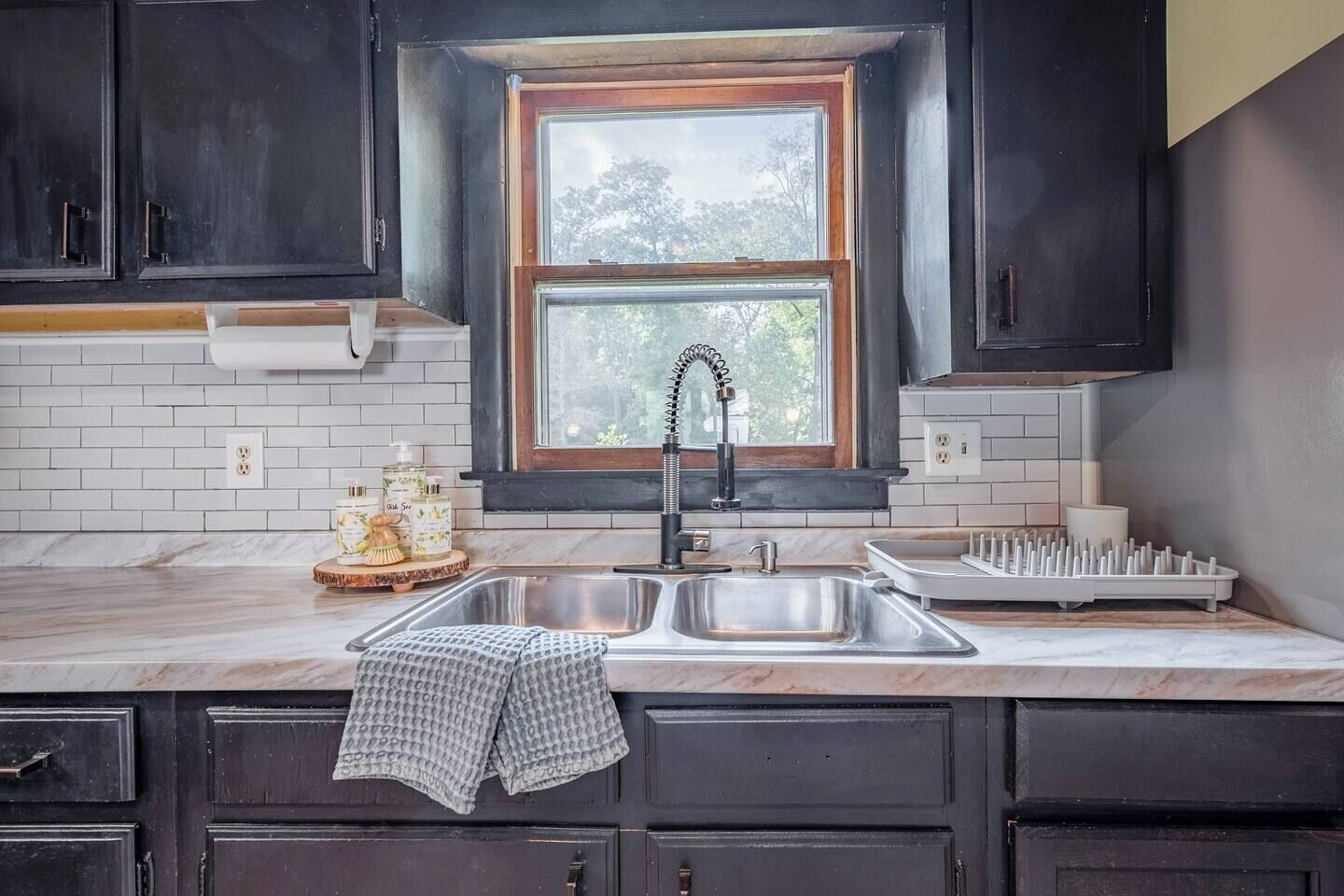 Una cocina con gabinetes oscuros, un lavamanos doble, una ventana con vistas y una encimera de mármol.