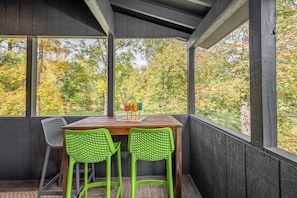 A covered outdoor seating area with a table and two chairs, overlooking a forested area.