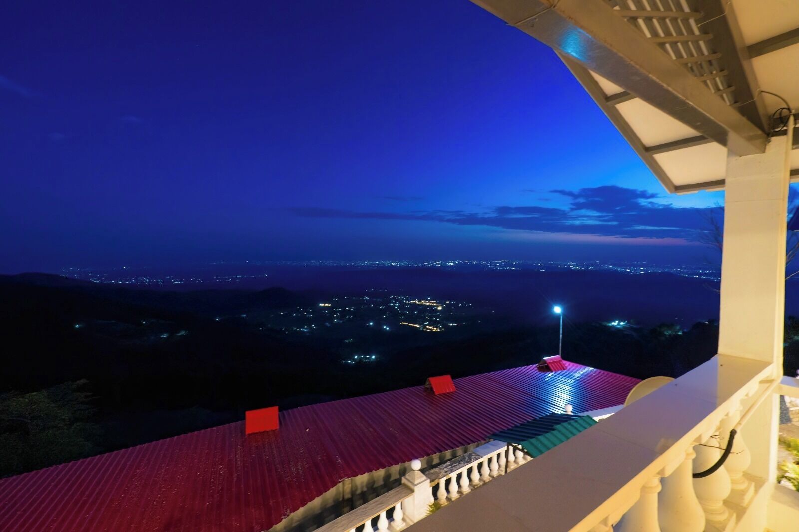Un balcon doté d’un toit rouge, d’où l’on a une vue sur le paysage urbain illuminé la nuit.
