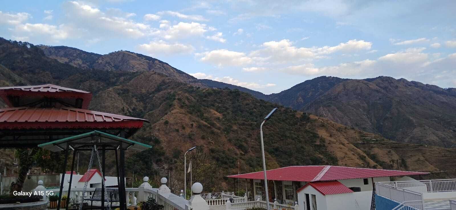A mountainous landscape with a building featuring a red roof and a covered area with a swing.