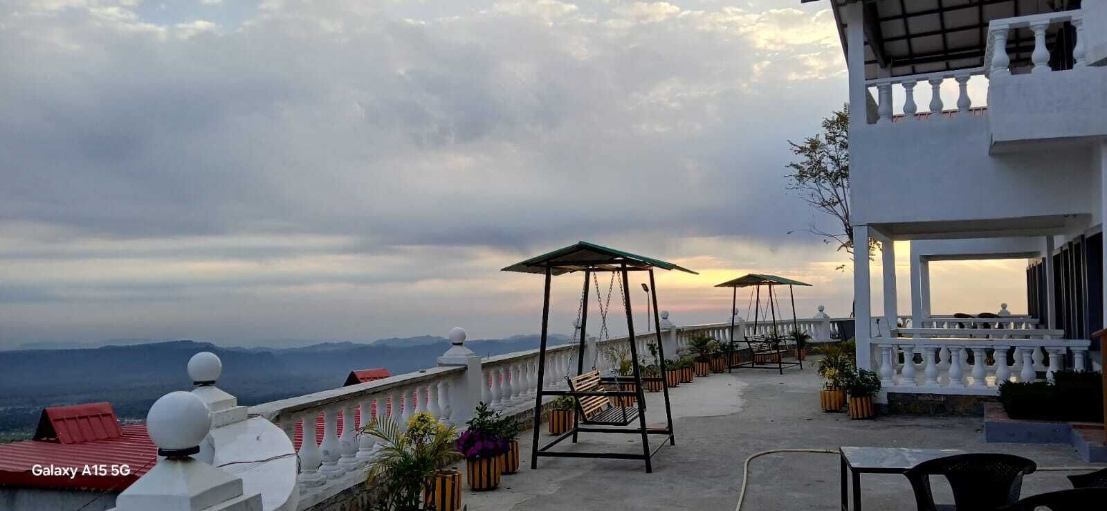 Eine Dachterrasse mit Bergblick, Sitzmöglichkeiten im Freien und ein weißes Gebäude mit Balkonen.