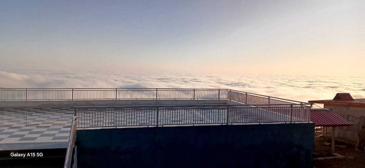 A rooftop terrace with a metal railing, a checkered floor, and a view of clouds below.