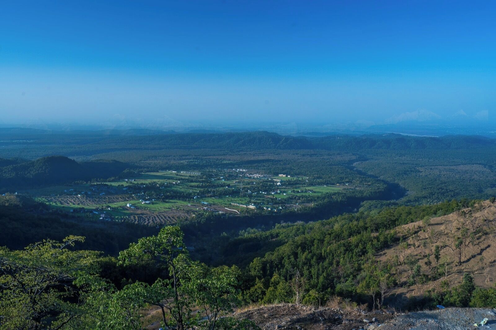 A panoramic view of a valley with scattered buildings, dense forests, and rolling hills.