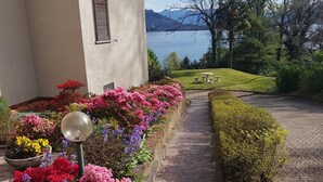 Un bâtiment qui offre une vue sur un lac et des montagnes. On y trouve des parterres de fleurs et un chemin pavé.