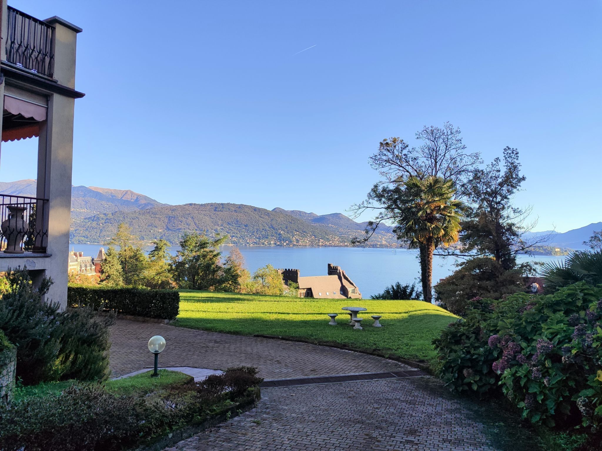 A garden with a paved path, a fountain, and a view of a lake and mountains.