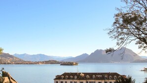 Un grand bâtiment doté de nombreuses fenêtres et d’un toit plat, situé près d’une étendue d’eau, avec des montagnes en arrière-plan.