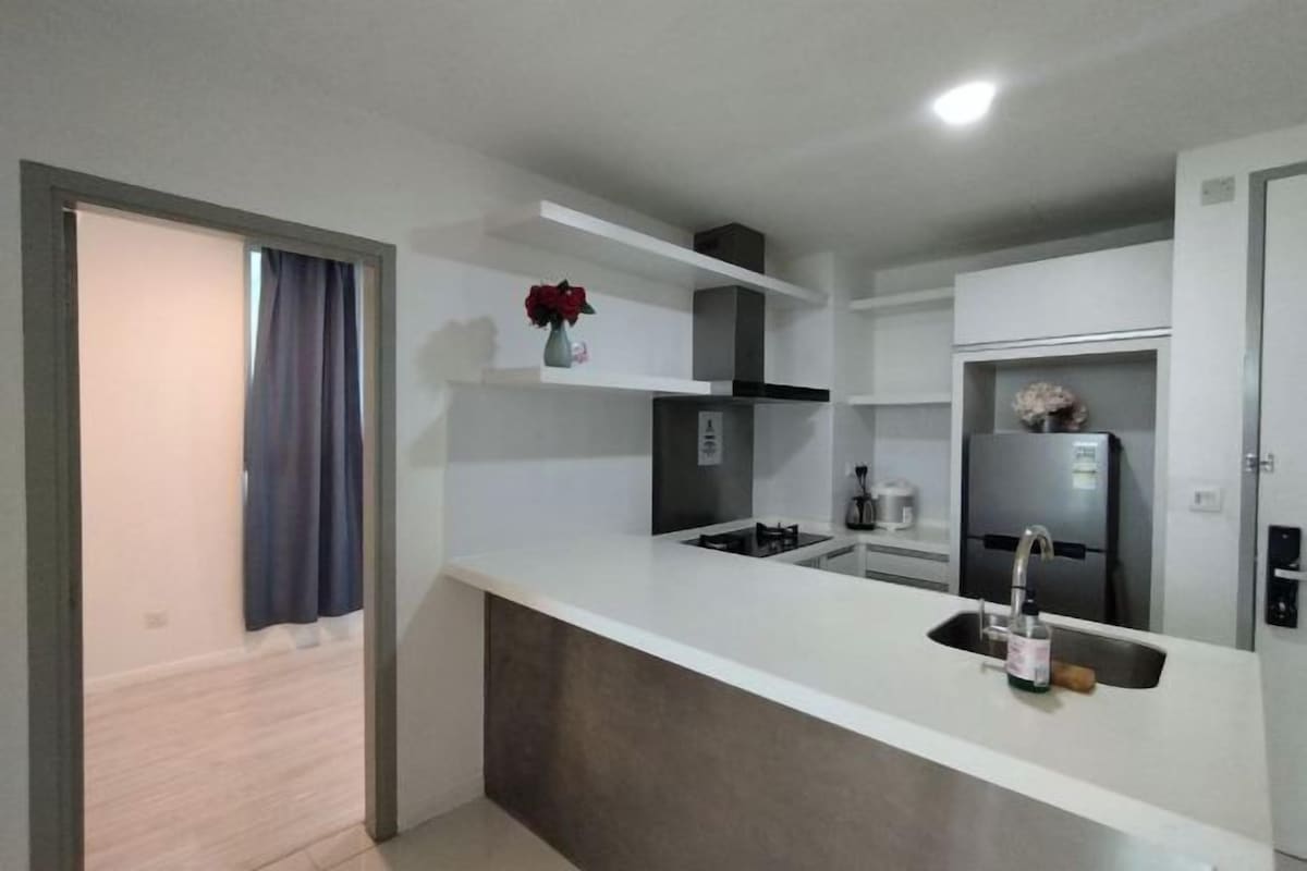 Una cocina moderna con encimera blanca, lavadero integrado y refrigerador de acero inoxidable.