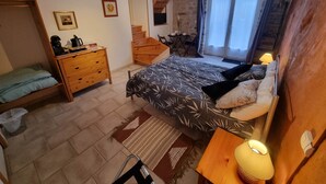 Een slaapkamer met een bed, een dressoir en een klein tafeltje met een lamp. Er is een raam met gordijnen en uitzicht op het omliggende landschap.