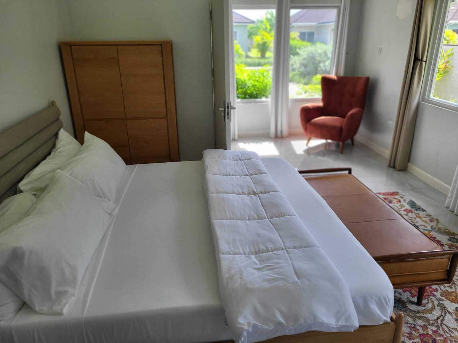 A bedroom with a bed, a wooden headboard, a red chair, and a view of greenery outside.